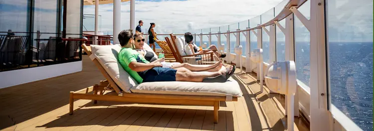 A group of people sunbathing on loungers on the deck of the Disney Wish cruise ship