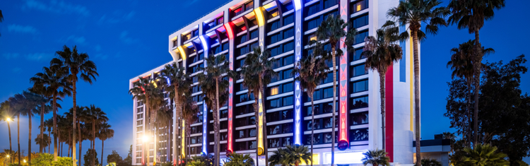 Pixar Place Hotel lit up at dusk with colorful vertical lights along the exterior