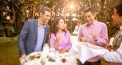 A Cast Member serving hors d'oeuvres to Guests standing around a cocktail table in a tropical garden