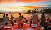 A group of Guests stand on a beach near banquet tables set for an elegant outdoor dinner