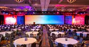 A ballroom with dining tables, a large screen, a stage and a podium