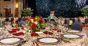 A ballroom with dining tables, floral arrangements, a stage, a podium and a backdrop featuring stars and fireworks