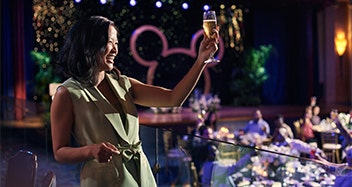 A businessperson raising her glass in a toast in front of colleagues at a ballroom with a large Mickey Mouse silhouette