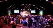 A Caribbean themed party in a large ballroom with many Guests sitting and standing at a variety of tables