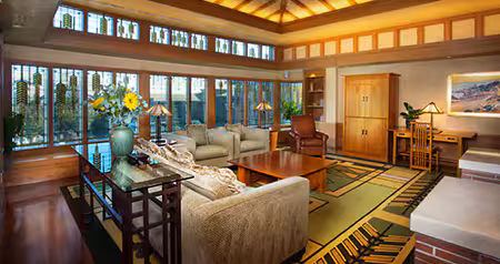 A spacious hotel suite with large windows, tall ceilings, sofas, wooden furniture and decorative rugs