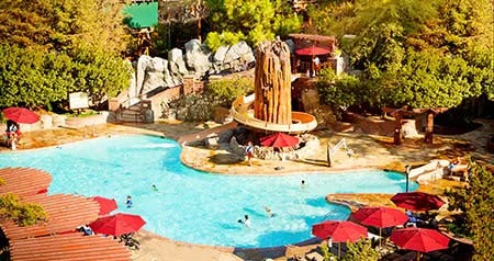 The Redwood Pool at Disney’s Grand Californian Hotel & Spa, with a slide winding around a rock structure surrounded by lounge chairs, umbrellas and trees