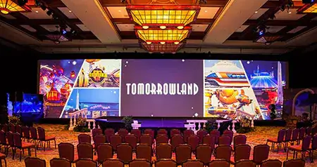 A conference room with rows of chairs facing a large ‘Tomorrowland’ display screen and images of attractions