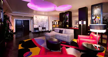 A hotel suite with a sofa, a chair, a geometric rug, an overhead Mickey ceiling light and panel artwork with Mickey Mouse sketches