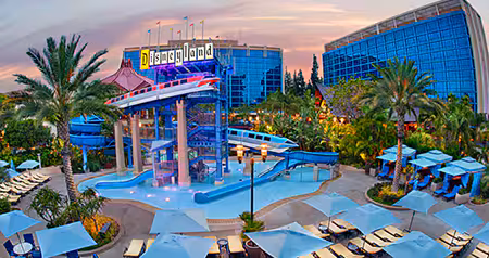 The pool area at the Disneyland Hotel with monorail themed water slides, lounge chairs, umbrellas and hotel towers at sunset