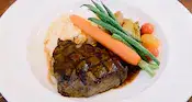 A plated entree featuring grilled steak with mashed potatoes, green beans, carrots, roasted potatoes and cherry tomatoes