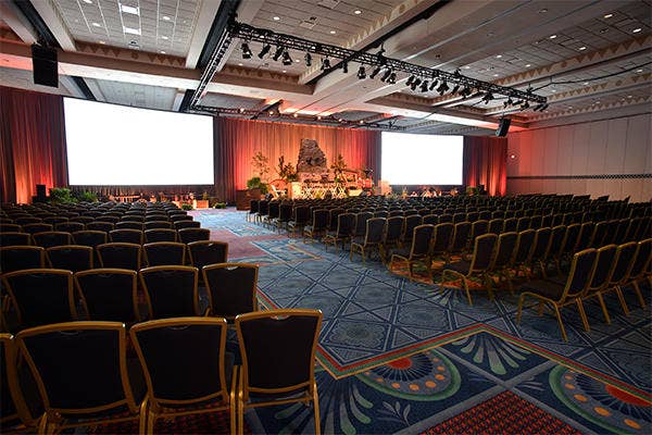 A large event space with theater style seating, 2 projection screens and a stage set for a presentation
