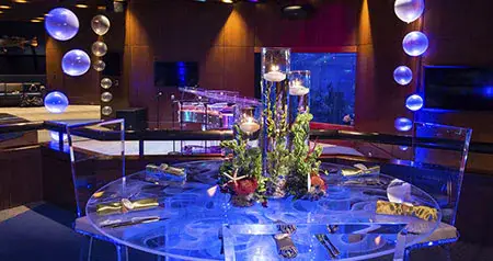 A table with floating candles near a stage and an aquarium in the Living Seas Salon at Epcot