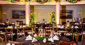 A ballroom filled with tables and chairs with Christmas trees, centerpieces, garlands and wreaths