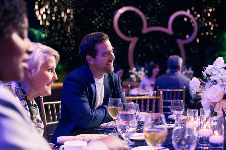 A man and woman smiling at an evening event with glasses of wine at their table