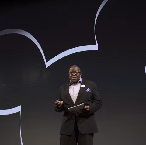 A man in a suit speaking in front of a large silhouette of Mickey Mouse