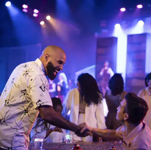 Two men shake hands at a table at an indoor evening event