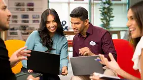 Four people working together in an office setting, 2 on laptops and 2 discussing something