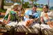 Two men and a woman sit side by side on chaise lounges on a beach