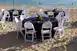 Eight banquet tables with beach chairs and Tiki torches by the water on a beach