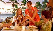 At an outdoor restaurant, a Cast Member serves a food platter to 3 Guests toasting with wine