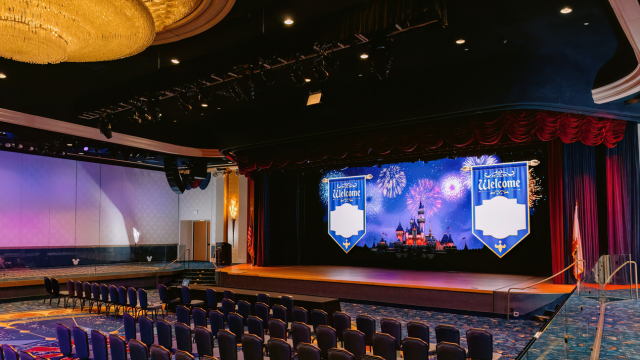 A theater style event venue with a stage and Sleeping Beauty Castle displayed on an LED wall
