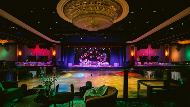 A grand ballroom with a chandelier, stage, dance floor and event lighting at Disneyland Hotel