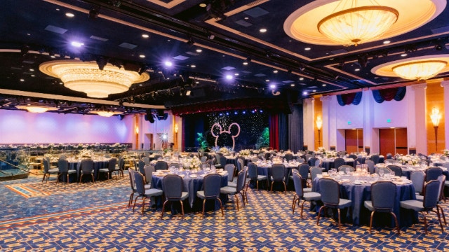 A grand ballroom set for a formal dinner with a Mickey ears stage display at Disneyland Resort