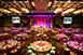 A ballroom with many fully set tables and a stage with large television screens on either side