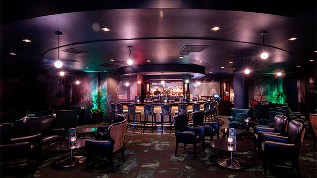 The interior of Broken Spell Louge at Disneyland Hotel with a circular bar, stools, armchairs and illuminated lights