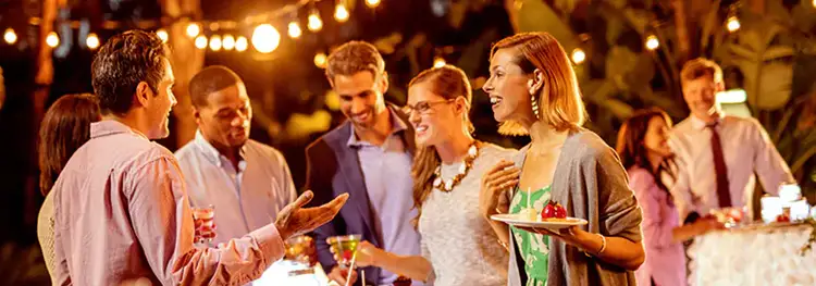 Attendees at an outdoor evening reception talking and enjoying food and drinks