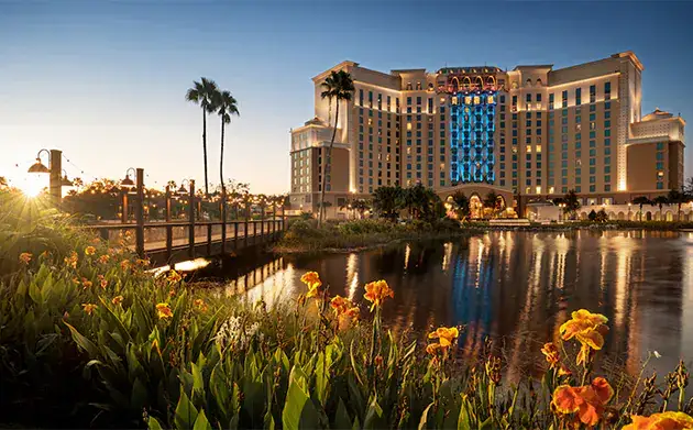 A walking bridge and lush landscaping is captured in a lakeside view of the reimagined Disneys Coronado Springs Resort.